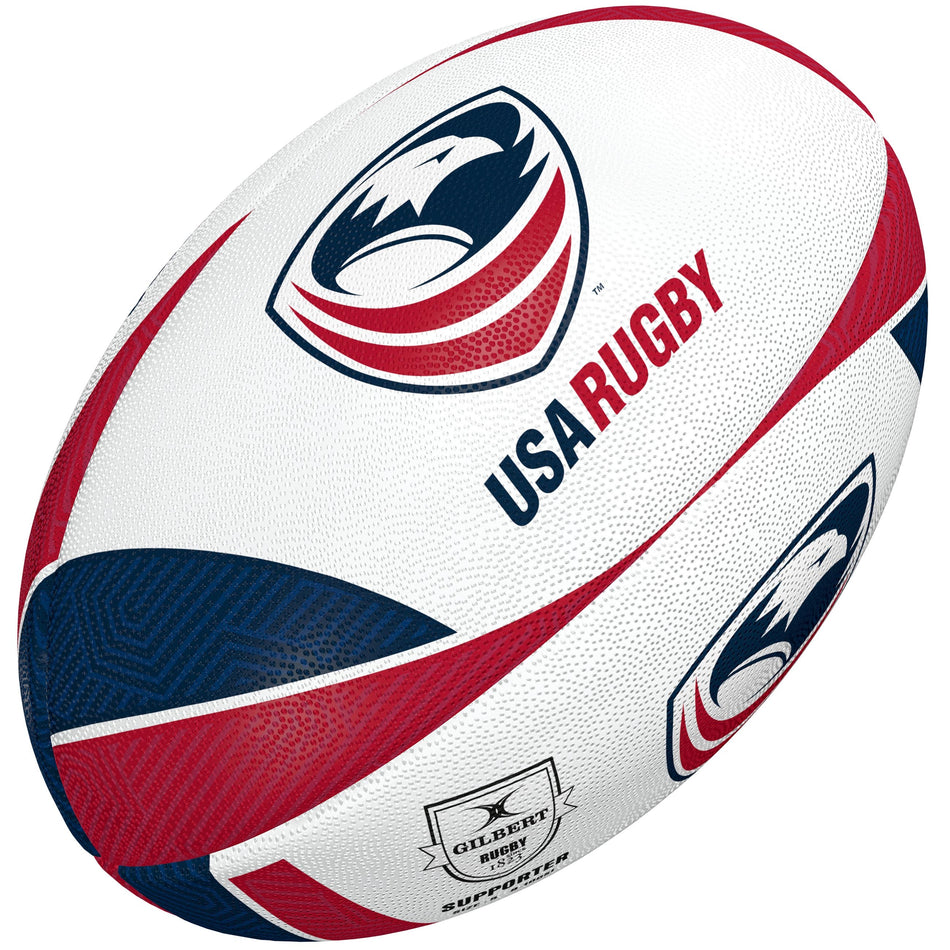 The Gilbert USA Supporter Rugby Ball is a white ball with red and blue accents, featuring the USA Rugby logo with a stylized eagle head and "USA RUGBY" text. The Gilbert logo adds authenticity—a great gift or collectible for rugby fans.