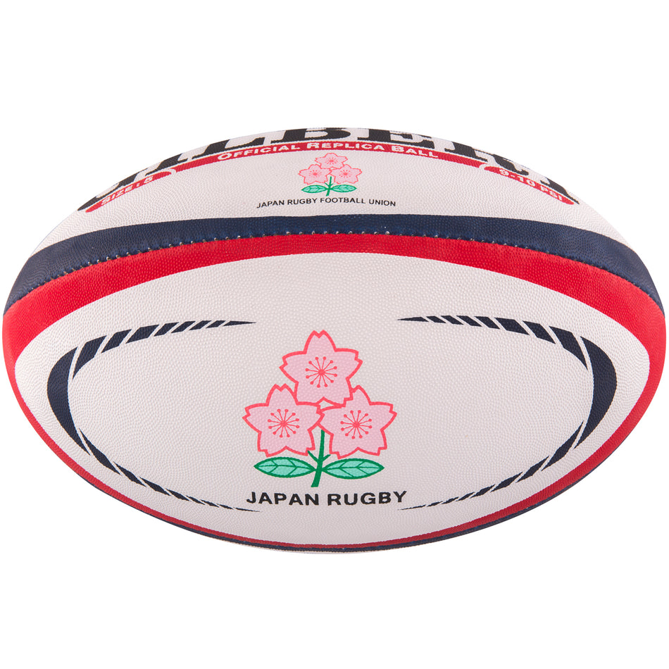 The Gilbert Japan Replica Rugby Ball by Gilbert is white with red and blue stripes, features two pink Cherry Blossoms with green stems, and has "JAPAN RUGBY" printed below the flowers.
