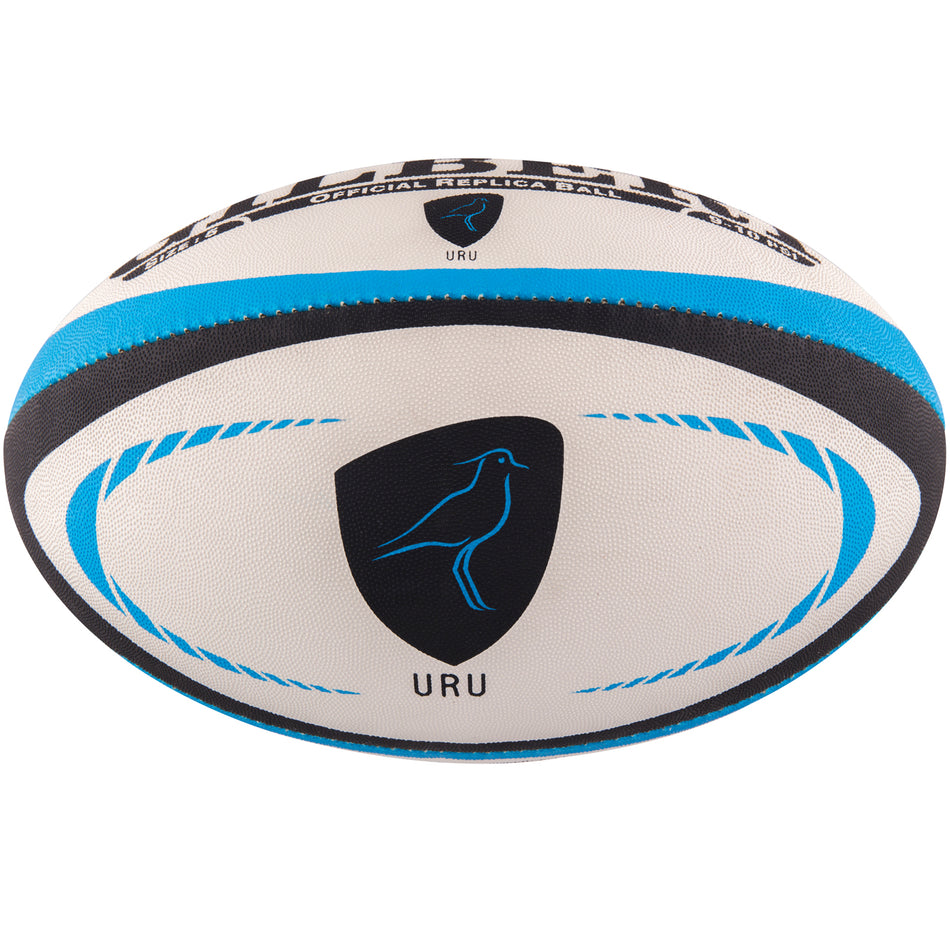 The Gilbert Uruguay Replica Rugby Ball by Gilbert is white with blue and black accents, featuring a black shield logo with a bird and URU text—perfect for Rugby World Cup 2023 fans.