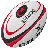 The Gilbert Saracens Replica Rugby Ball is a white ball with red and black accents, featuring the SARACENS name, red star and crescent logo, and partial Gilbert branding—ideal for Gallagher Premiership Rugby fans.