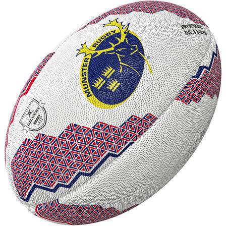 The Gilbert Munster Supporters Rugby Ball by Gilbert features red and blue geometric patterns, a textured white surface, the Munster Rugby stag logo on one side, and a small silver badge—perfect memorabilia for any fan.