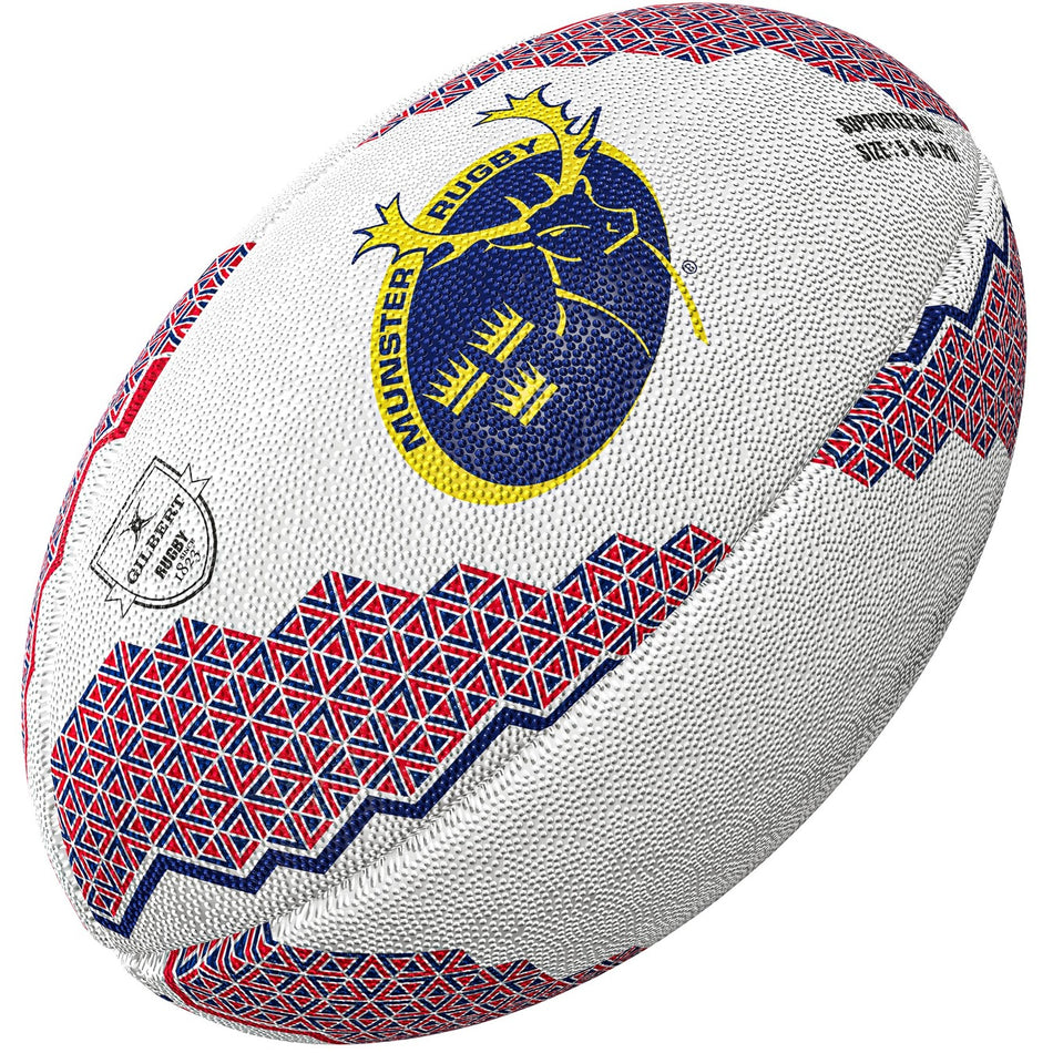 The Gilbert Munster Supporters Rugby Ball by Gilbert features red and blue geometric patterns, a textured white surface, the Munster Rugby stag logo on one side, and a small silver badge—perfect memorabilia for any fan.