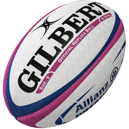 A close-up of the Gilbert Allianz Replica Rugby Ball, mainly white with blue and pink accents, featuring GILBERT and Allianz branding. Its textured surface makes it ideal for women's rugby training and matches.
