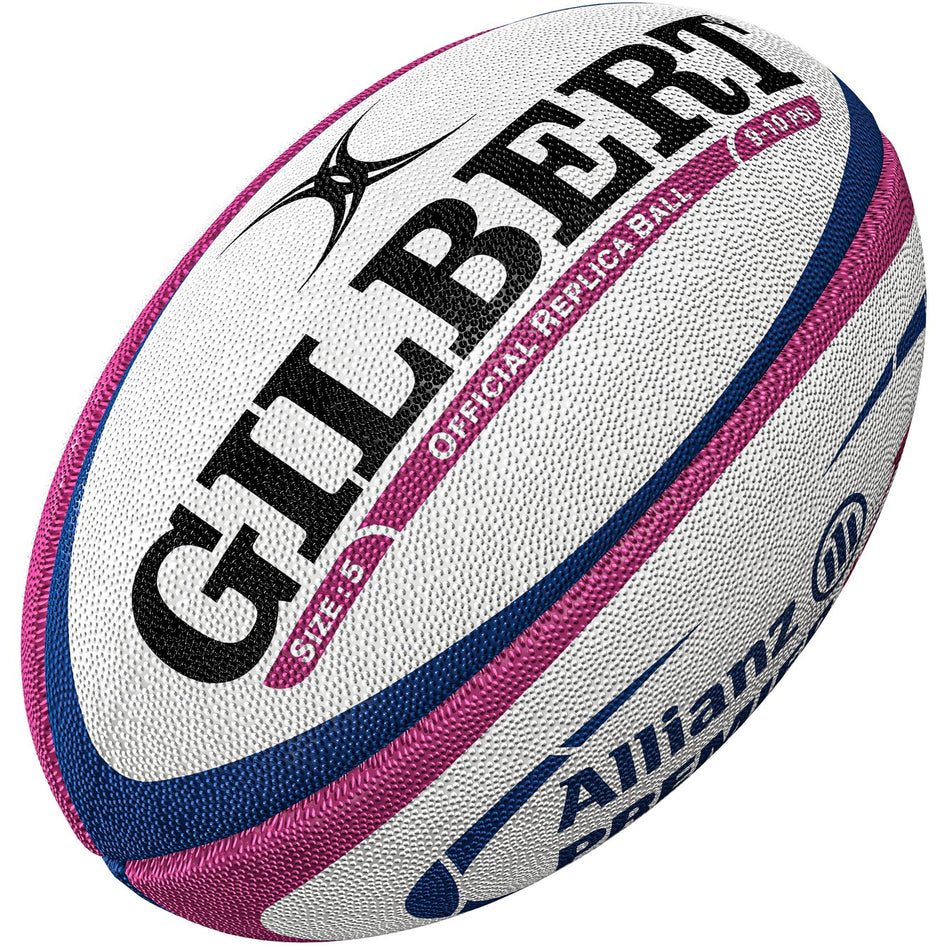 A close-up of the Gilbert Allianz Replica Rugby Ball, mainly white with blue and pink accents, featuring GILBERT and Allianz branding. Its textured surface makes it ideal for women's rugby training and matches.