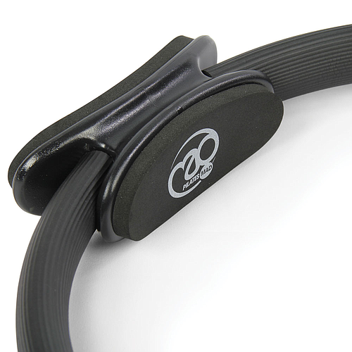 A close-up of the Fitness Mad Pilates Ring - Double Handle in black, with padded side handles and the “Fitness Mad” logo on one pad, set against a plain white background—ideal for toning exercises.