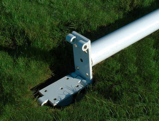A Harrod Sport Aluminium Rugby Post featuring hinge adaptors lies on green grass with its base partly embedded, and bolts visible on the detached mounting plate, indicating an issue during erection.