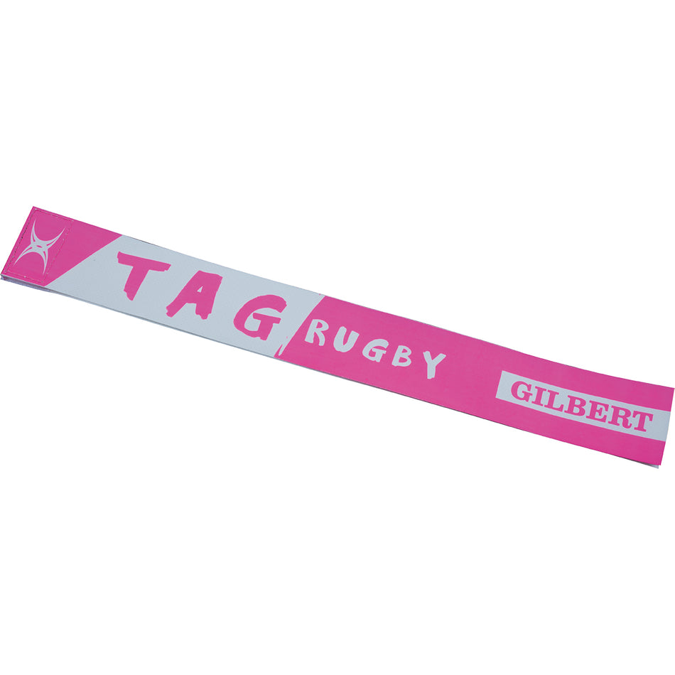 The Gilbert Tag Rugby Belt by Gilbert is a pink and white rectangular strip featuring TAG RUGBY and GILBERT print with a small logo on the left end—ideal as a training aid for non-contact tag rugby games.