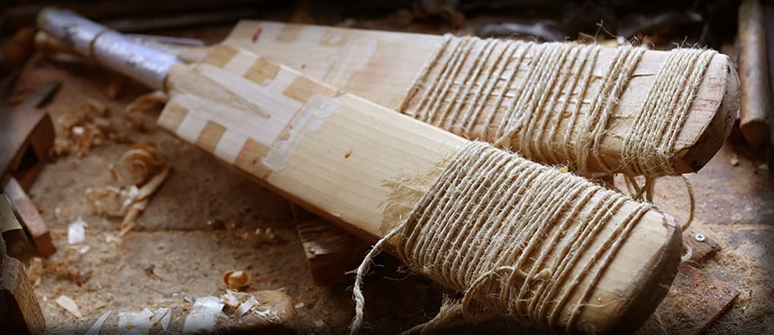 Two unfinished cricket bats with twine-wrapped handles lie amid wood shavings and tools, evoking expert repair in progress—Martin Berrill Sports’ Cricket Bat Repair (Toe, Shoulder & Edge).