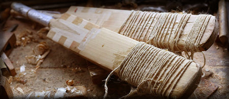 Two unfinished cricket bats with twine-wrapped handles lie amid wood shavings and tools, evoking expert repair in progress—Martin Berrill Sports’ Cricket Bat Repair (Toe, Shoulder & Edge).