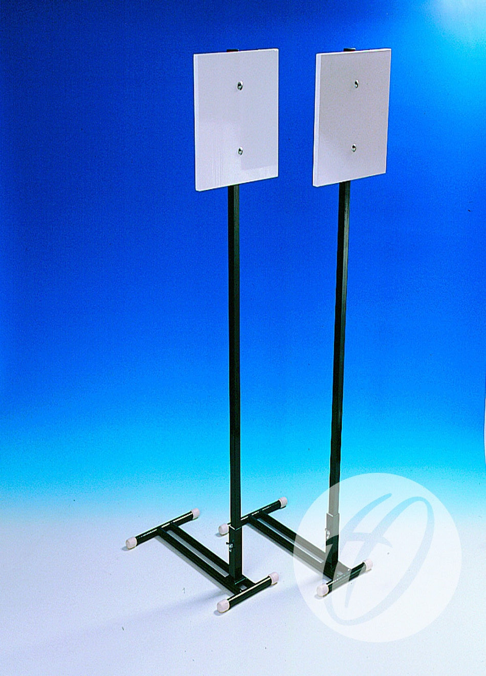 Two Harrod Sport Stoolball Wickets feature square white panels atop steel stands with T-shaped bases and white caps, set against a gradient blue background—ideal for cricket pitches or as official Stoolball equipment.