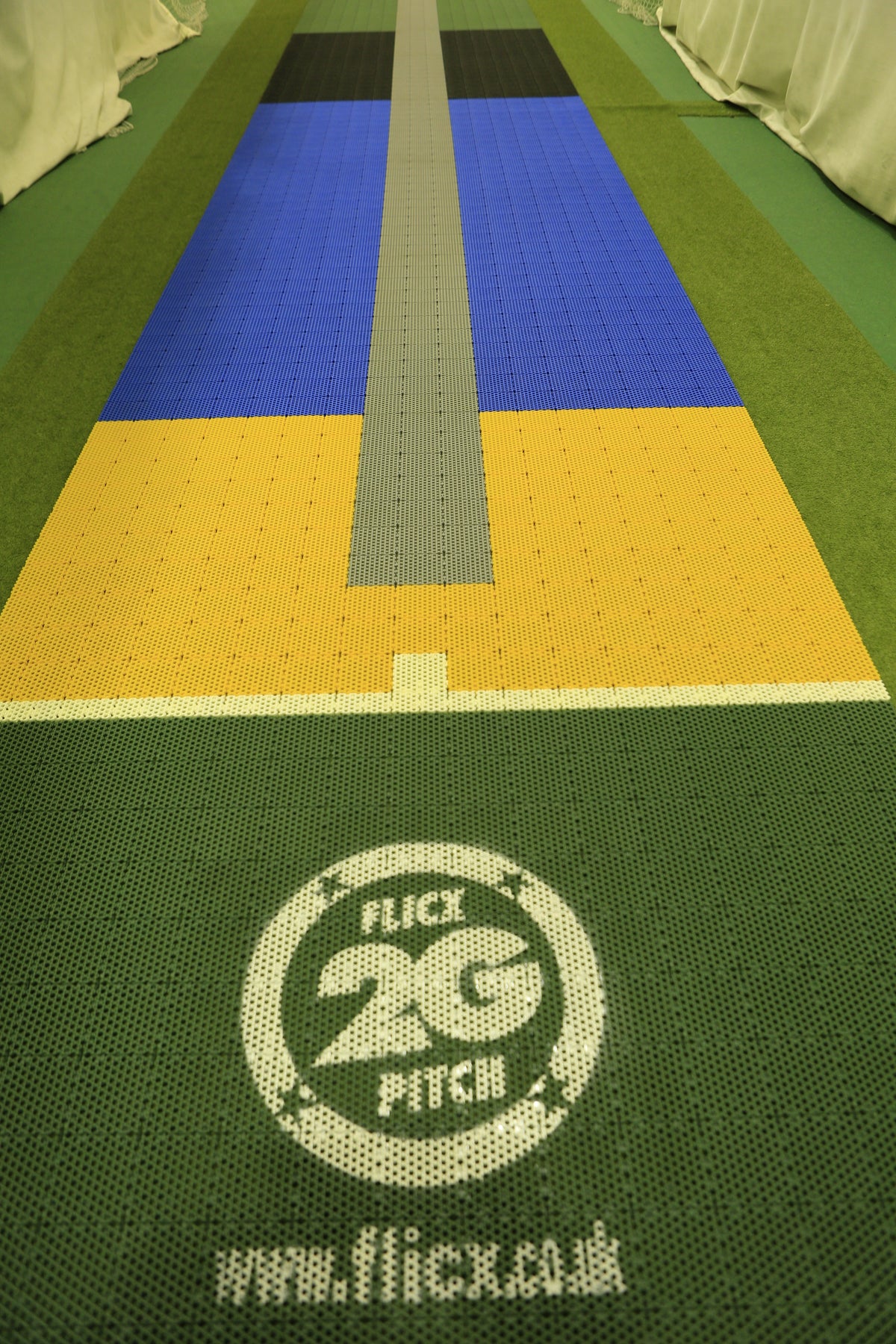 A close-up of a multicolored 2G Flicx Skills & Eagle Eye Pitch by Flicx UK, showing the central strip, branding, website text, and coaching aid details printed on the green front surface.
