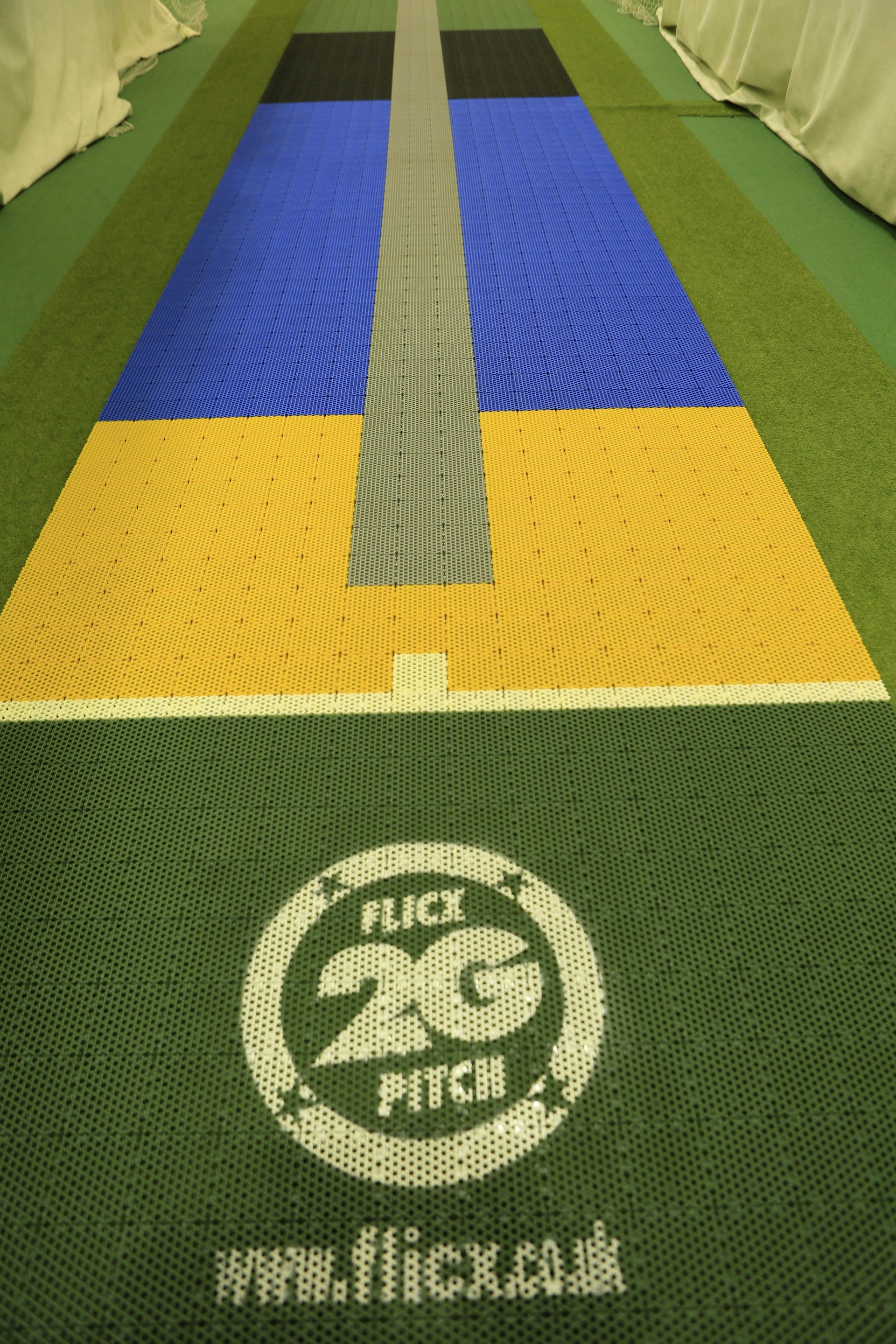 A close-up of a multicolored 2G Flicx Skills & Eagle Eye Pitch by Flicx UK, showing the central strip, branding, website text, and coaching aid details printed on the green front surface.