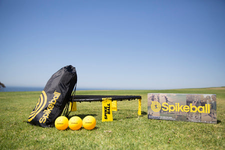 The Kankakee Spikeball Standard Set includes an adjustable net on a round frame, three yellow balls, a black and yellow carry bag with branded tags, and comes in the official Spikeball box—perfect for outdoor games on grass.