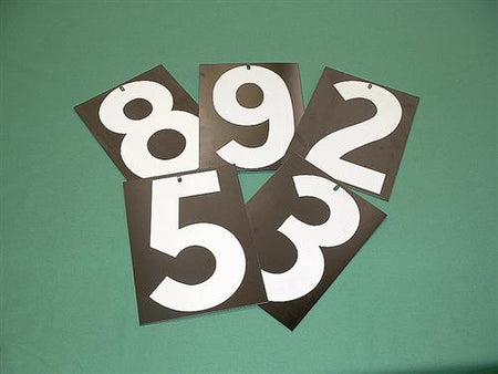 Five R J Hill Engineering Whole Number Plates (9 x 12) showing large white numbers 8, 9, 2, 5, and 3 on black plastic are fanned out on a green surface. Each has a small hole at the top center for easy handling.