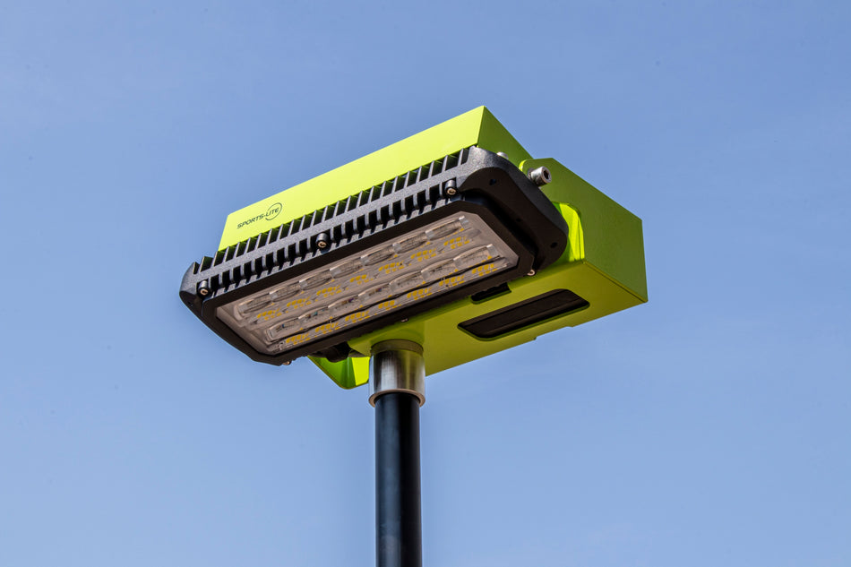 A close-up of the Ritelite Sports Lite Light Head Unit, a modern green street light with optimized optical lensing, shown mounted on a black pole against a clear blue sky.