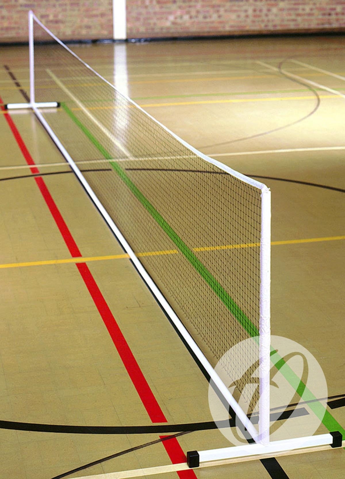 A Harrod Sport Freestanding Practice Mini Tennis Net is set up indoors on a gym floor with colorful court lines and a brick wall behind, supported by sturdy Harrod Sport Mini Tennis Posts.