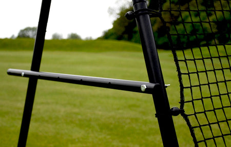 Close-up of a Precision Pro Jumbo Rebounder by Precision Training, featuring a black frame (9ft x 7ft) set on grass, with a blurred green field and trees in the background under a cloudy sky.