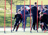 A group of boys in sportswear weave between Precision Training’s Precision Boundary Poles (Set of 12) with ground spikes on a grassy field, practicing lateral drills while others wait for their turn.
