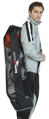 A man in a gray tracksuit carries a Precision Training Precision Tubular 5 Ball Bag, a large black mesh bag filled with soccer balls, over his shoulder.