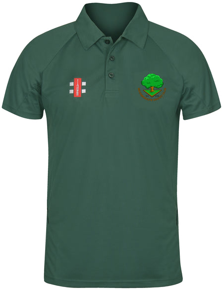 The Woodmancote CC Matrix V2 Polo Shirt by Gray Nicolls is a dark green, short-sleeved training polo with a collar, featuring a red and white logo on the right chest and a circular green tree emblem on the left. Excellent moisture management.