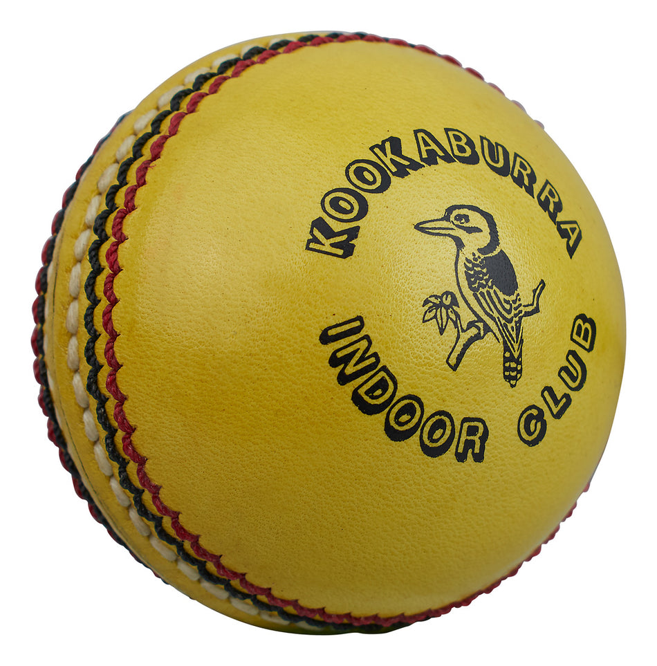 A close-up of the Kookaburra Indoor Club Cricket Ball, a yellow indoor cricket ball with red and black stitching, featuring the Kookaburra logo and a kookaburra bird illustration.