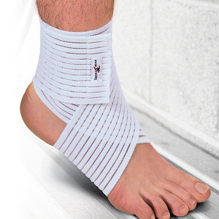 A close-up of a foot and ankle wearing the Precision Training Precision Elasticated Ankle/Elbow Wrap - Universal, a white elastic support with horizontal straps for adjustable compression, against a blurred background.