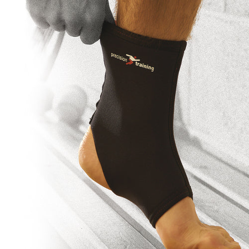 A person pulls a Precision Training Precision Neoprene Ankle Support onto their foot, emphasizing ankle support for injury recovery or sprains. The background is blurred and mostly grayscale.