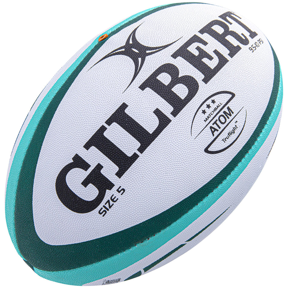 The Gilbert Atom Match Ball is a white and teal Size 5 rugby ball with black "GILBERT" and "ATOM" text, teal and green side stripes, a star rating, and is ideal for match play.