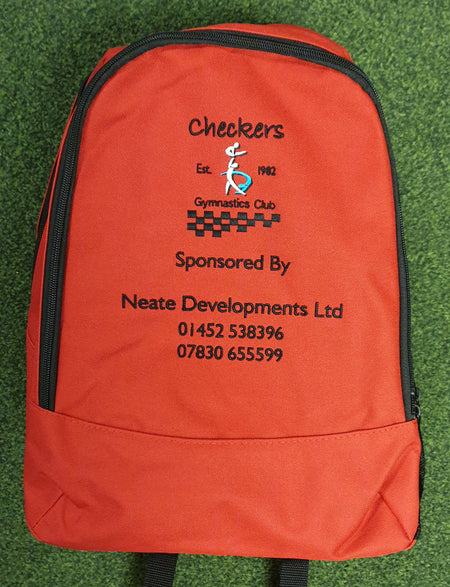 The PenCarrie Checkers Gymnastics Rucksack is a red 18L bag with embroidered club logo, sponsor details, and phone numbers in black and orange, plus a padded back panel, shown on green carpet.