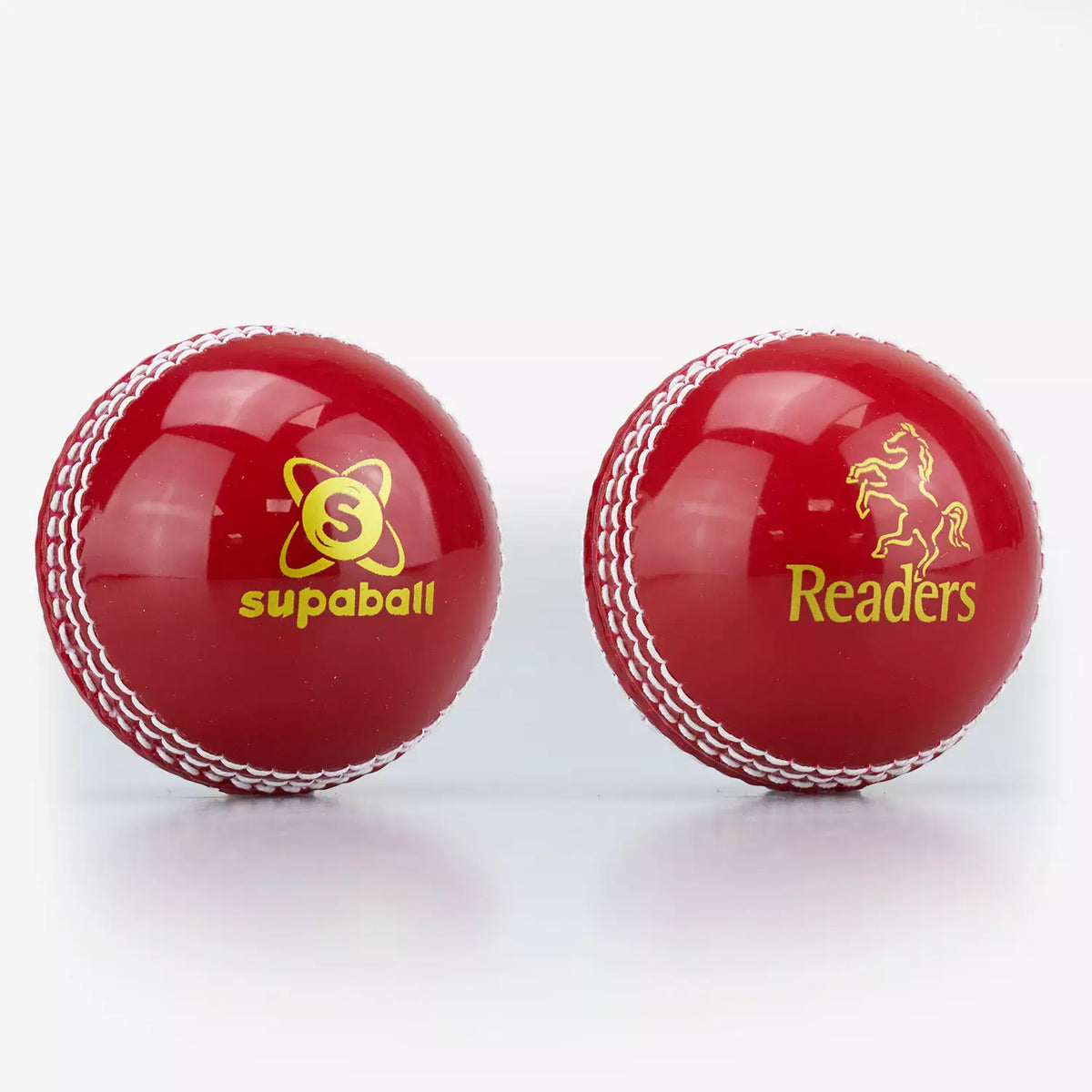 Two shiny red Readers Supaball cricket balls with white stitching and yellow horse logos are displayed side by side.