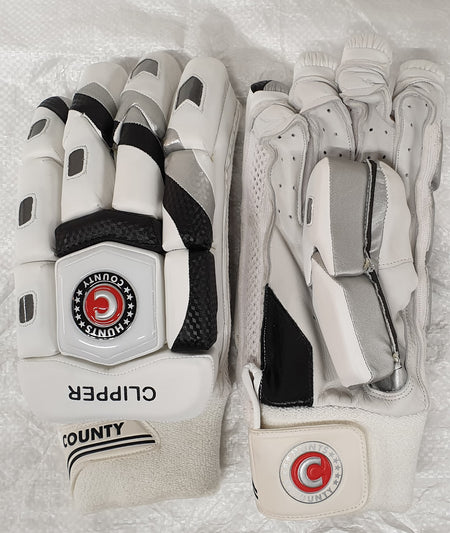 The Hunts County Clipper Batting Glove features a white split-finger design with black and silver accents, COUNTY branding, red and black wrist logo, calf leather palm, extra protection, and is shown on a textured white surface.