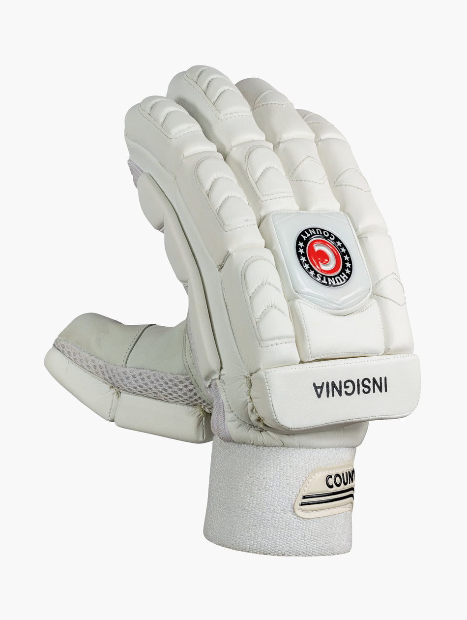 The Hunts County Insignia Batting Gloves are white, made from premium leather with padded fingers and knuckles for protection. They feature a black and red COUNTYS INSIGNIA logo on the back and 'INSIGNIA' near the wrist strap.