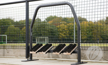 The Harrod Sport Freestanding Angled Boot Wipers feature multiple rows of stiff, angled brushes, making them ideal as convenient boot cleaning stations beside fenced sports fields with grass and trees in the background.