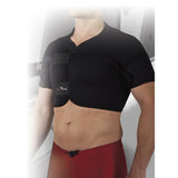 A person wears the Precision Training Precision Neoprene Full Shoulder Support with adjustable front-fastening straps over their upper body, paired with red shorts. The blurred gray background highlights relief from frozen shoulder.