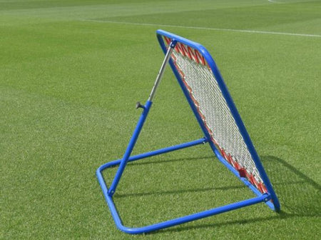 A Samba Sports Pro Rebounder with a blue frame and red accents is positioned on a green sports field, perfect for ball training drills and first touch practice.