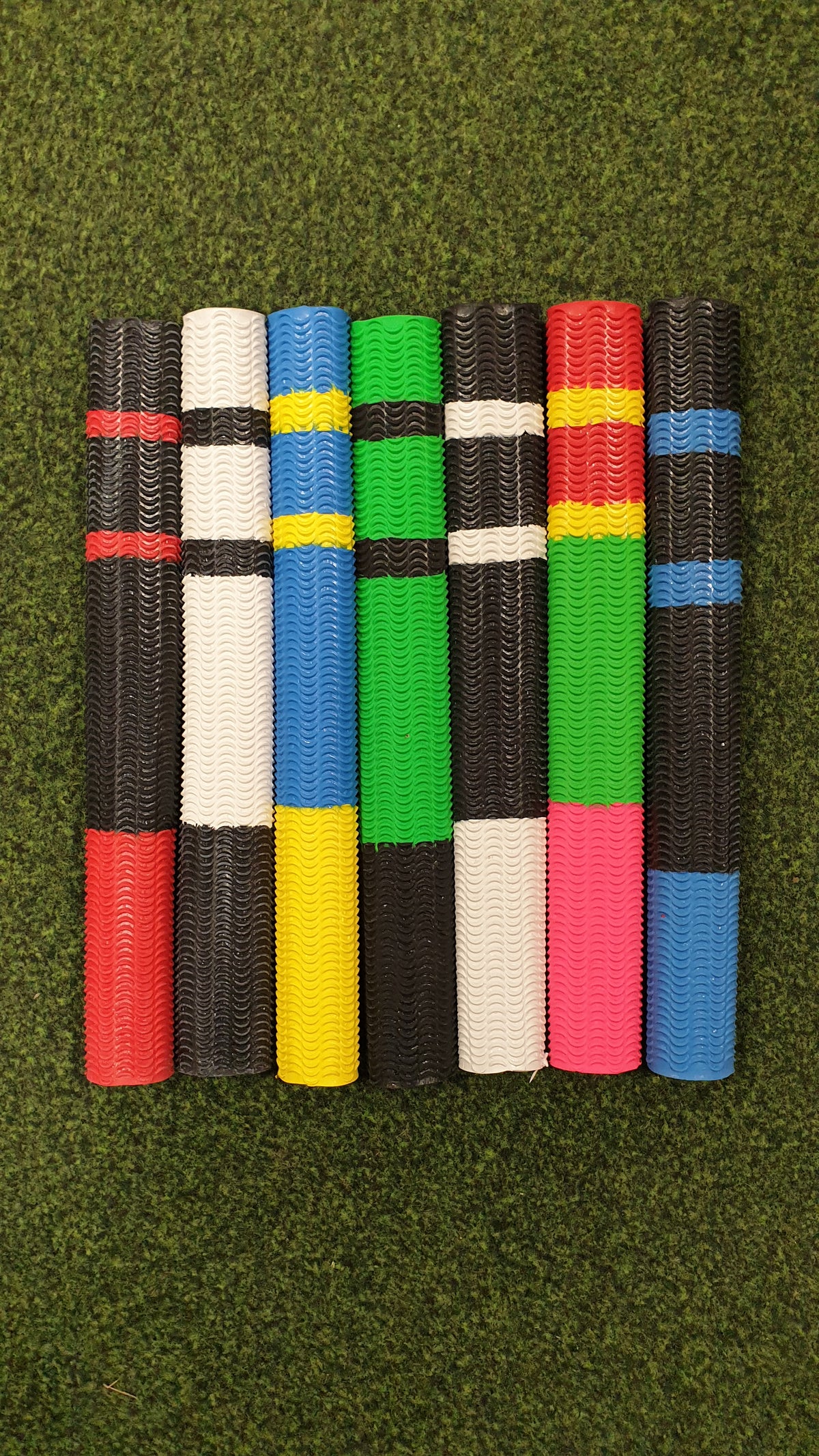Seven Hunts County Aqua Two Tone Bat Grips are arranged vertically on a grass-like surface, showcasing their vibrant two-tone designs and non-slip performance.
