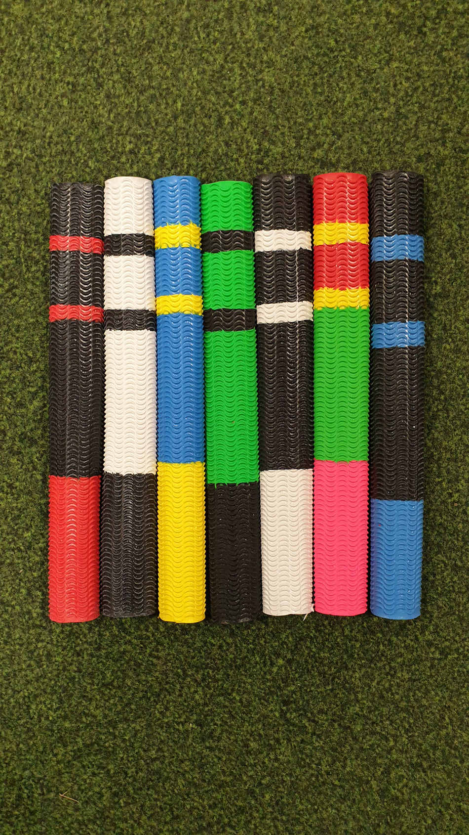 Seven Hunts County Aqua Two Tone Bat Grips are arranged vertically on a grass-like surface, showcasing their vibrant two-tone designs and non-slip performance.