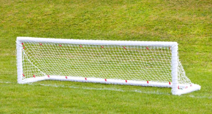 A pair of Samba Sports 8ft x 2ft Mini Hockey Goals stands on a grassy field, with more grass and a slight hill in the background.