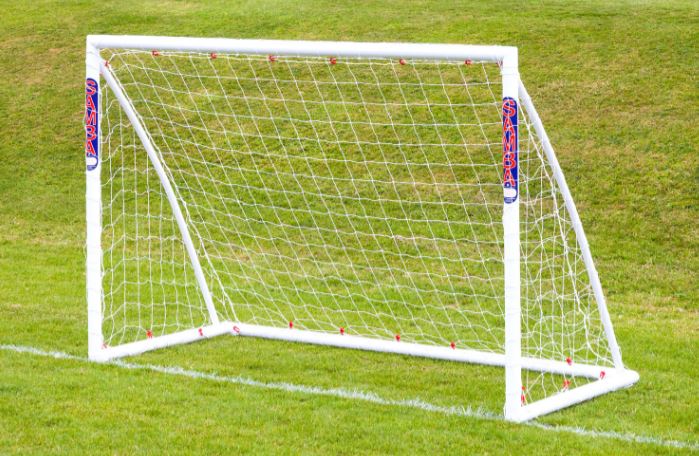 A 7'10 x 5'3 Mini Handball Goal by Samba Sports, made from shatterproof uPVC with a durable net, stands on green grass. "SAMBA" is printed in blue and red on both posts. The goal area is empty with no players present.