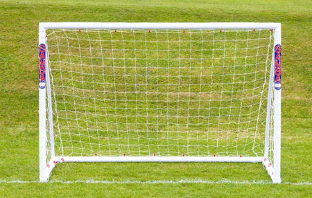A 7'10 x 5'3 Mini Handball Goal by Samba Sports, featuring a shatterproof uPVC frame and net, stands on a green field. The white posts display SAMBA SPORTS branding in red and blue, with visible horizontal lines in the background.