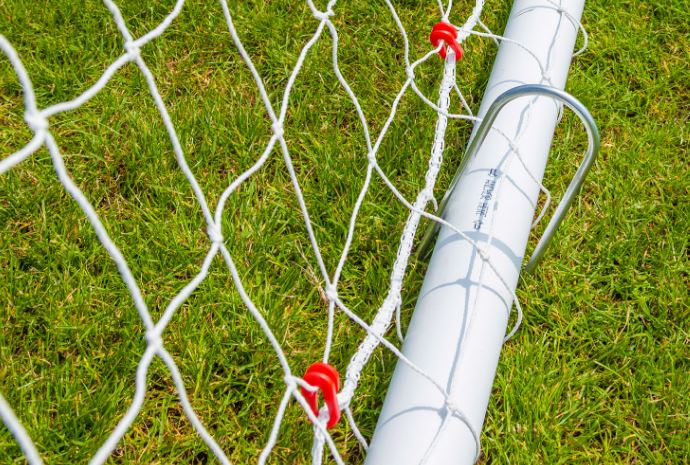Close-up of a Samba Sports 8ft x 2ft Mini Hockey Goal post on green grass, with white net attached using red clips. Details of the net, metal post, and grass textures are visible. Sold as a pair.