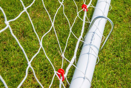 Close-up of a Samba Sports 7'10 x 5'3 Mini Handball Goal’s white net and red clips on green grass, highlighting its shatterproof uPVC frame and secure locking system in bright sunlight.