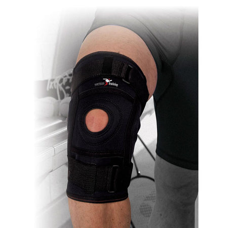 A person wears the Precision Training Precision Neoprene Hinged Knee Support, a black knee brace with adjustable straps and open patella design, providing medial and lateral knee support.