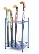 Four field hockey sticks with different colored accents stand upright in a freestanding blue powder-coated steel Mastersport Hockey Stick Rack with two shelves. Each stick has a black shaft, wooden curved end, and "MASTERPLAY" printed on it.