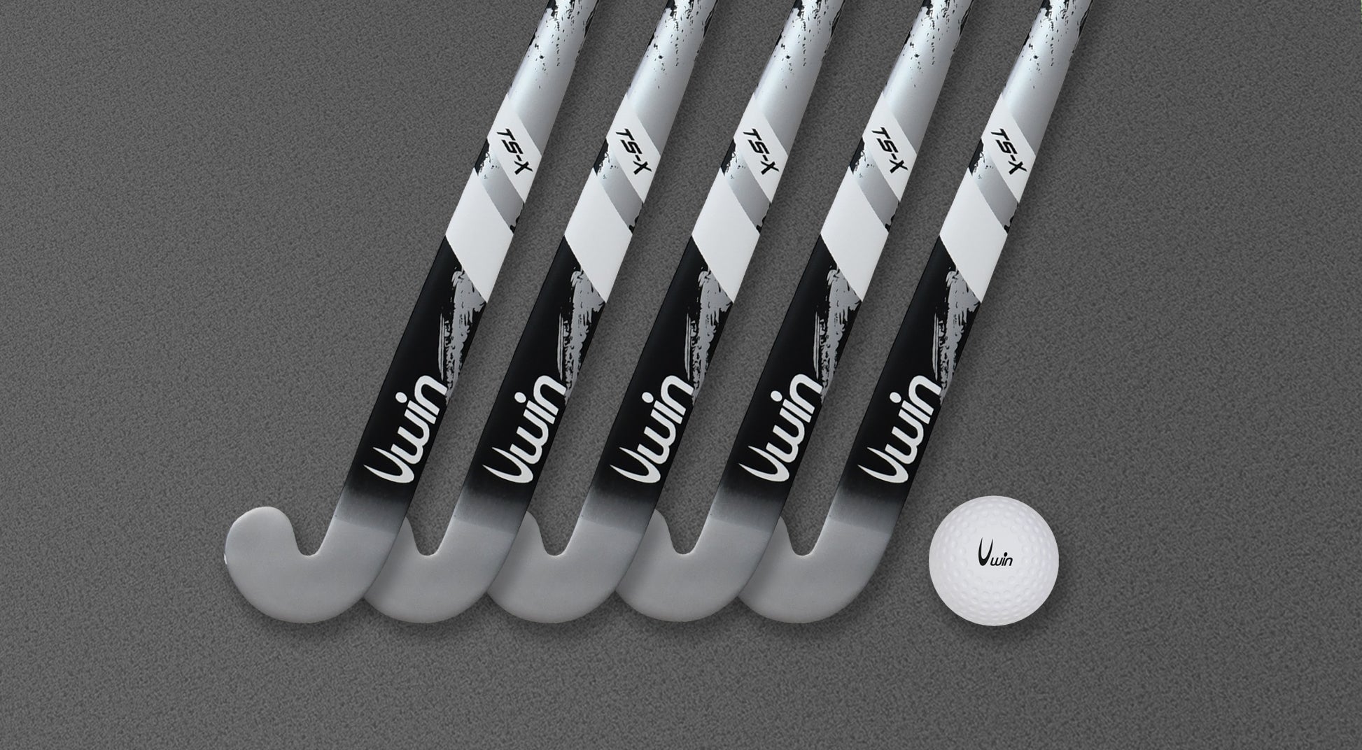 Five metallic silver and black Uwin TS-X hockey sticks from Uwin are lined up diagonally on a gray textured surface. A white field hockey ball, also bearing the Uwin logo, sits to the right of the sticks.