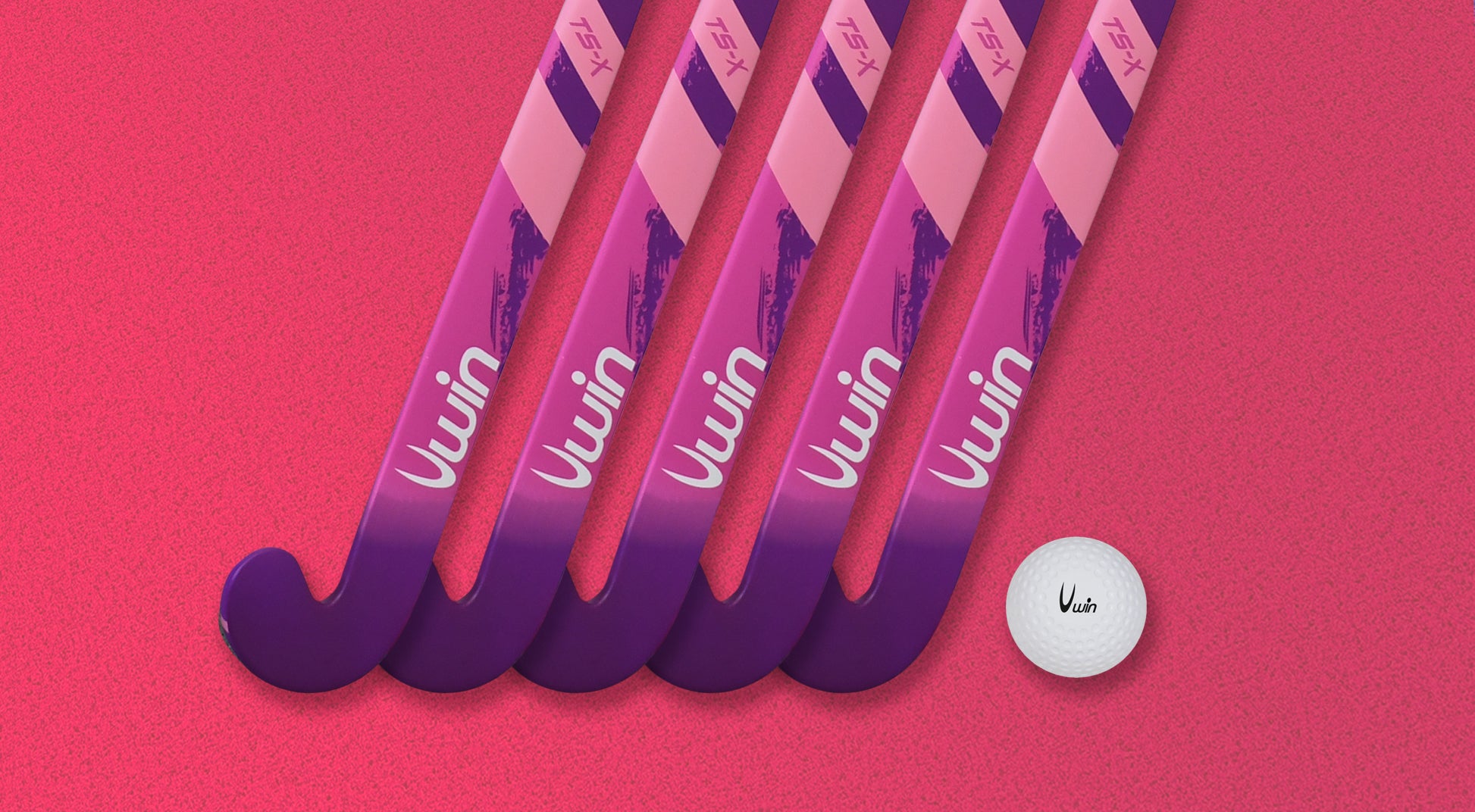Five Uwin TS-X Hockey Sticks in pink and purple are arranged diagonally on a textured pink surface, with a white field hockey ball placed nearby.