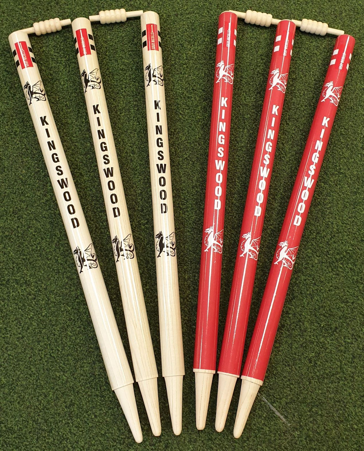 Four light wooden and two red Custom Printed Club Cricket Stumps by Gray Nicolls, featuring the brand’s horse logo and "KINGSWOOD", are set on green artificial grass with a wooden bail resting on the first two stumps.