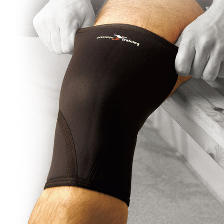 A person pulls the Precision Training Precision Neoprene Knee Support, in black, onto their knee while sitting on a bench for added arthritis relief.