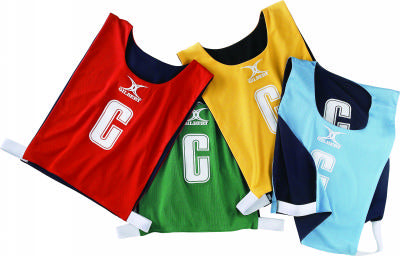 Gilbert Reversible Netball Bibs by Gilbert are shown in red, green, yellow, and light blue, overlapped. Each team bib displays a large white "C" on the front.
