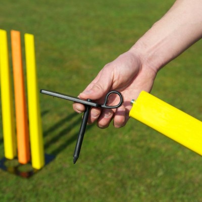 A hand holds the Fusion Single Stump and a black fixing tool from Fusion, highlighting this durable cricket training aid, with two yellow Fusion multi-stumps visible on green grass in the background.